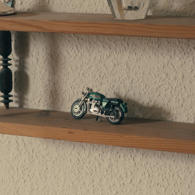 Eine Nahaufnahme eines kleinen Wandregals aus Holz, auf einem Brett steht ein grünes Miniaturmotorrad. 